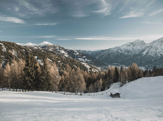 Spuren im Schnee an einem Berg mit Aussicht auf den verschneiten Lienzer Talboden.