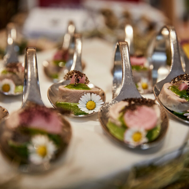 Haubenküche im Gannerhof - Gericht bestehend aus einem runden Fleischstück mit einer grünen Soße verziert mit einem Gänseblümchen auf einem Löffel angerichtet.