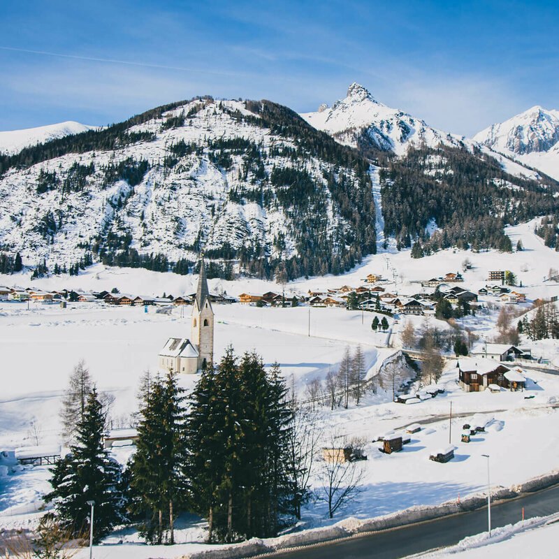 Blick auf das verschneite Kals mit Kirche und Wohnhäusern, an einem sonnigen Tag.
