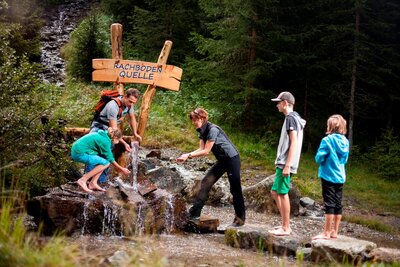 Eine Rangerin des Nationalpark Hohe Tauern bei einer Wanderung auf dem Wassererlebnisweg in St. Jakob i. D.. Gerade machen sie bei einer Wasserquelle Halt, um sich mit dem klaren Wasser zu erfrischen.