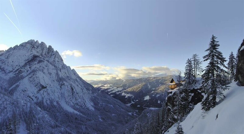 Die Dolomitenhütte liegt auf dem Felsen umgeben von einer traumhaften Winterlandschaft mit viel Schnee und blauem Himmel.