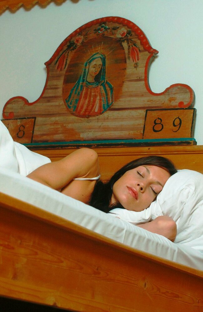 Eine Frau schläft in einem Bett mit weißem Bettbezug aus der Ameisenperspektive.