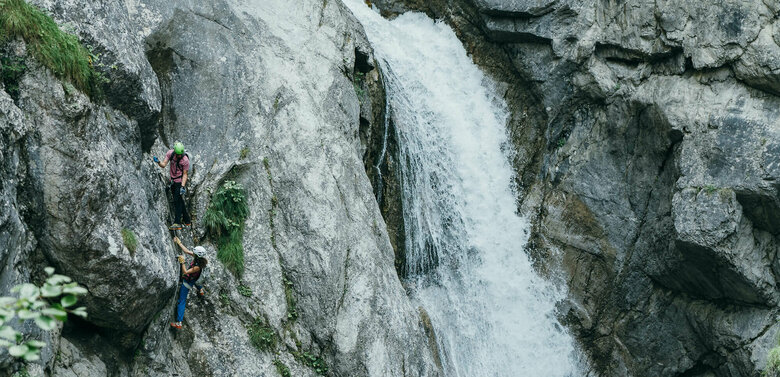 Zwei Personen auf einem Klettersteig neben einem Wasserfall in der Galitzenklamm.