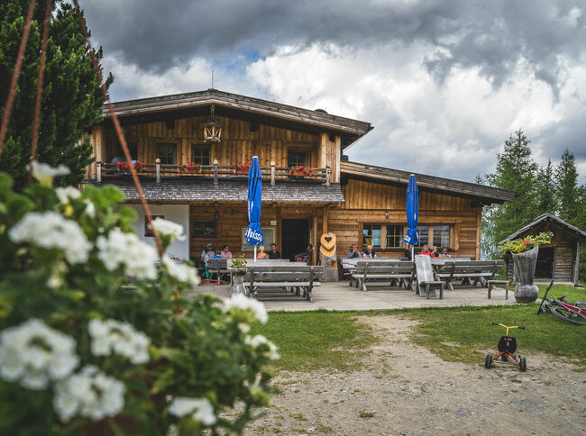 Blick auf die urige Leckfeldalm, mit Gaesten auf der Terrasse.