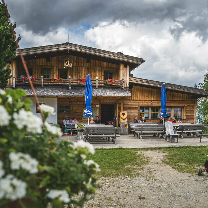 Blick auf die urige Leckfeldalm, mit Gaesten auf der Terrasse.