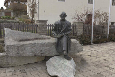 Der Reimmichlbrunnen in St. Veit i. D.. Eine Statue des legendären "Reimmichls" aus einem Metall gefertigt, in einer sitzenden Position auf dem aus Stein gefertigten Brunnen.