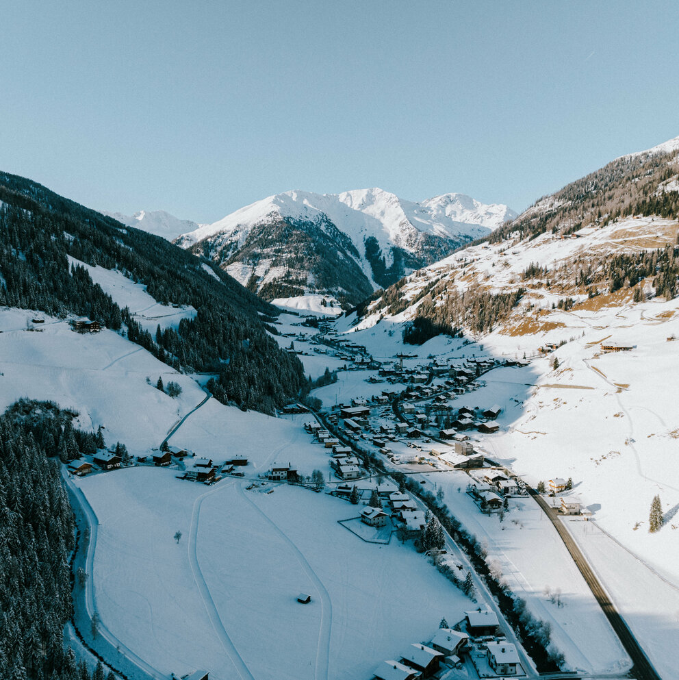 Luftaufnahme von dem mit Schnee bedeckten Dorf Innervillgraten an einem traumhaften Wintertag.