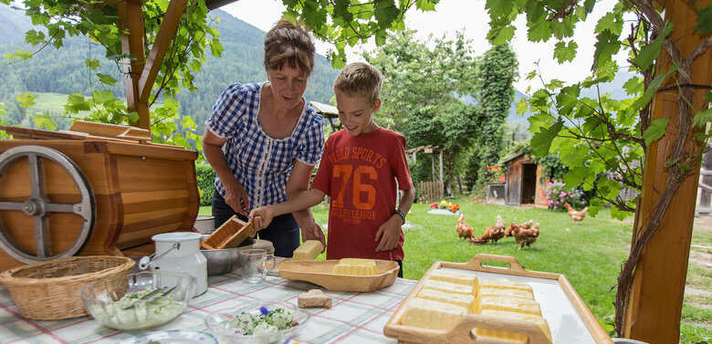 Eine Frau und ein Junge bereiten Butter im Garten des Klampererhofs zu.