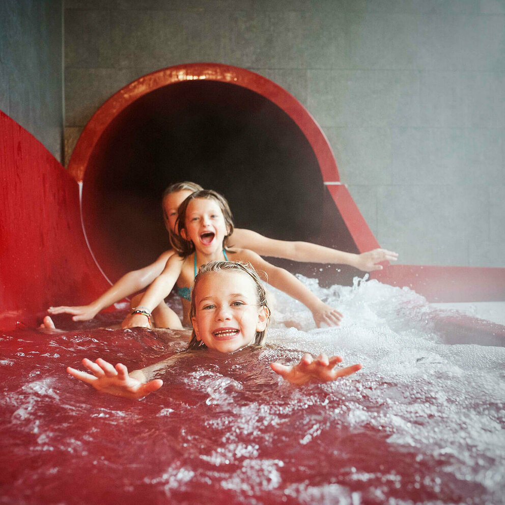 Drei Mädchen am Ausgang einer roten Wasserrutsche im Dolomitenbad in Lienz.