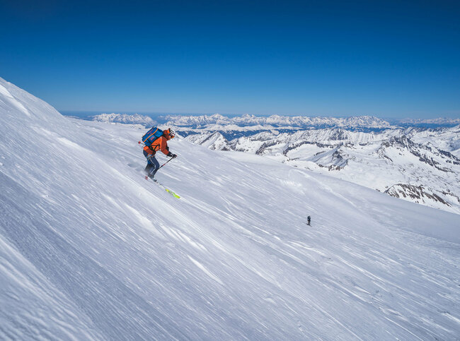Ein Skifahrer bei der Abfahrt Richtung Venedigerscharte mit Bergkulisse und blauem Himmel.