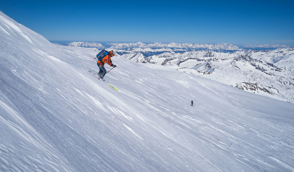 Ein Skifahrer bei der Abfahrt Richtung Venedigerscharte mit Bergkulisse und blauem Himmel.