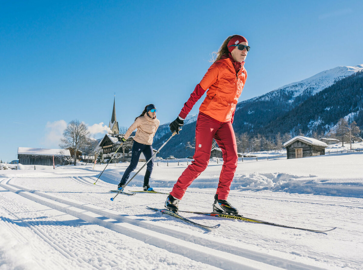 Zwei Langläuferinnen bei perfekten Bedingungen im sonnigen Defereggental mit Ortsansicht.