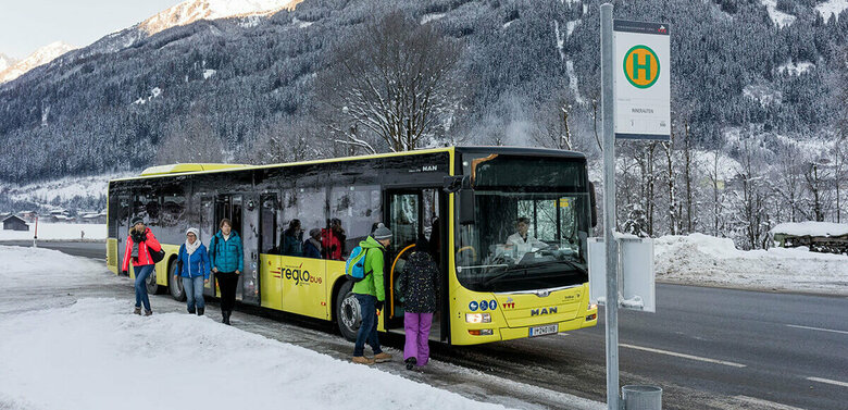 Gelber Bus hält an einer Bushaltestelle im Winter und lässt Fahrgäste ein- und aussteigen.