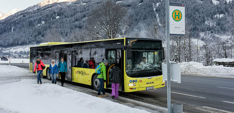 Gelber Bus hält an einer Bushaltestelle im Winter und lässt Fahrgäste ein- und aussteigen.