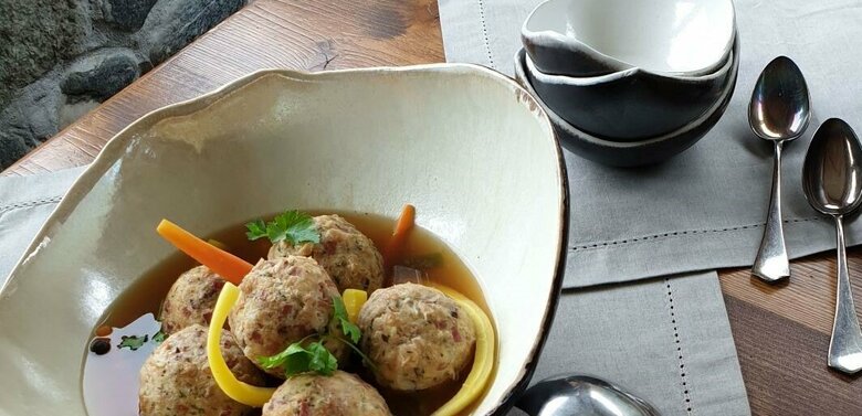 Aufnahme von einer großen Schale mit Knödelsuppe. Daneben einige kleine Schalen und Löffel.