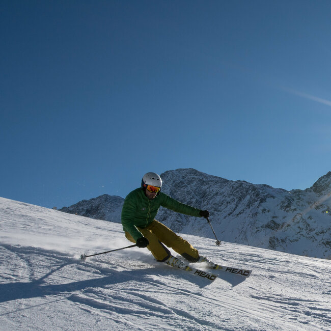 Ein Skifahrer mit grüner Jacke und gelber Hose carvt mit der Sonne im Rücken im Skigebiet Zettersfeld.