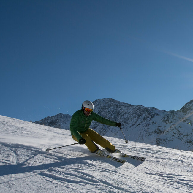 Ein Skifahrer mit grüner Jacke und gelber Hose carvt mit der Sonne im Rücken im Skigebiet Zettersfeld.