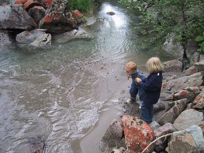 Kinder auf dem Wasserwanderweg im Bergwasserparadies Defereggental. Sie stehen am Ufer eines Baches und blicken in den niedrigen, von Fels umgebenen Wasserspiegel.