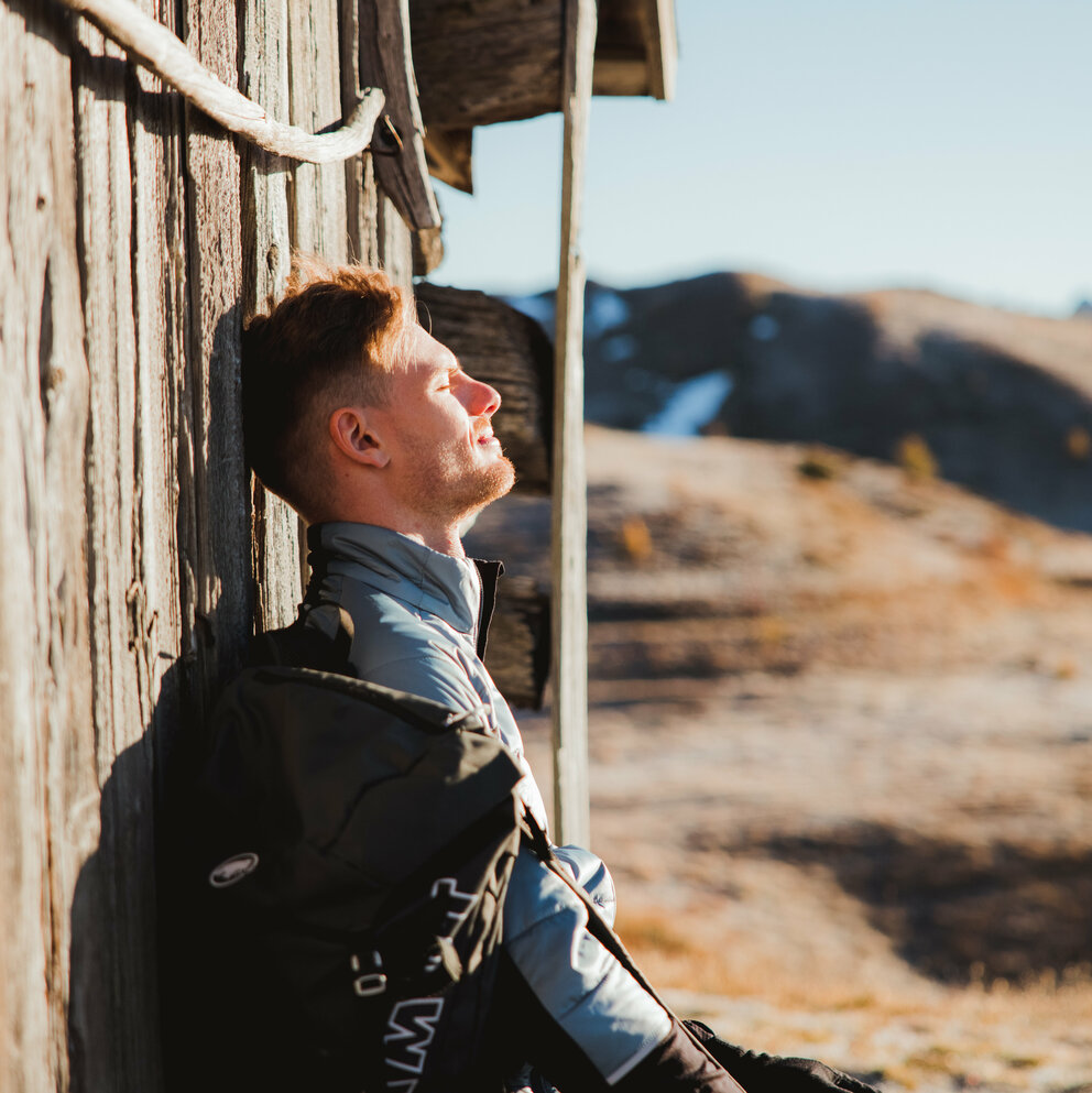 Wanderer genießt die wärmende Sonne bei einer alten Heuhütte der Kutteschupfen