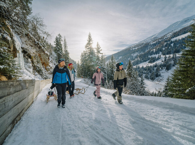 Eine Familie in Schianzügen unterwegs auf der Rodelbahn im verschneiten Winkeltal in Außervillgraten, Osttirol.