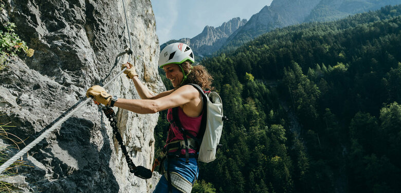 Eine Frau mit Helm und Rucksack hängt mit Kletterausrüstung im Galitzenklamm Klettersteig.