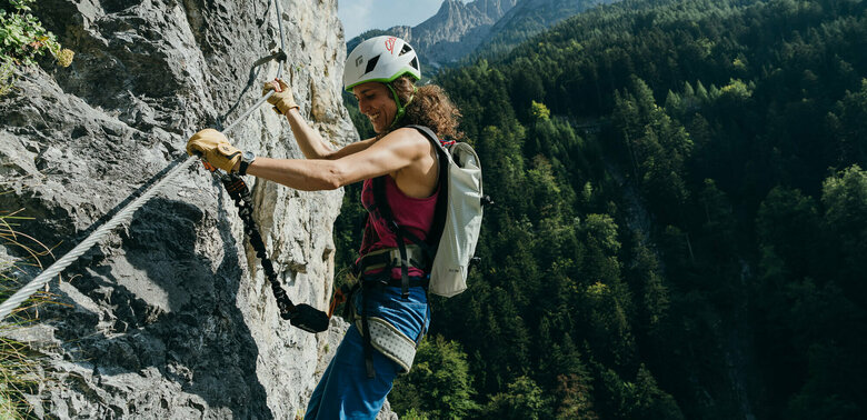 Eine Frau mit Helm und Rucksack hängt mit Kletterausrüstung im Galitzenklamm Klettersteig.