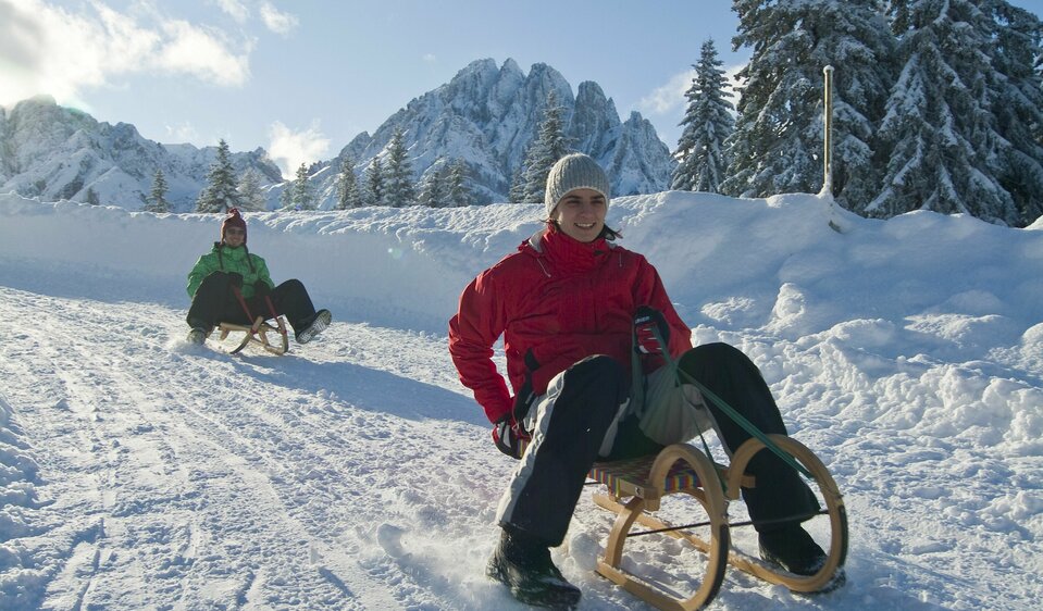 Zwei Personen rodeln über die Rodelbahn von der Dolomitenhütte hinunter ins Tal.