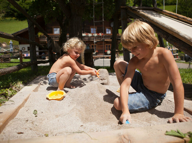 Zwei Kinder spielen im Sand auf einem Bauernhof.