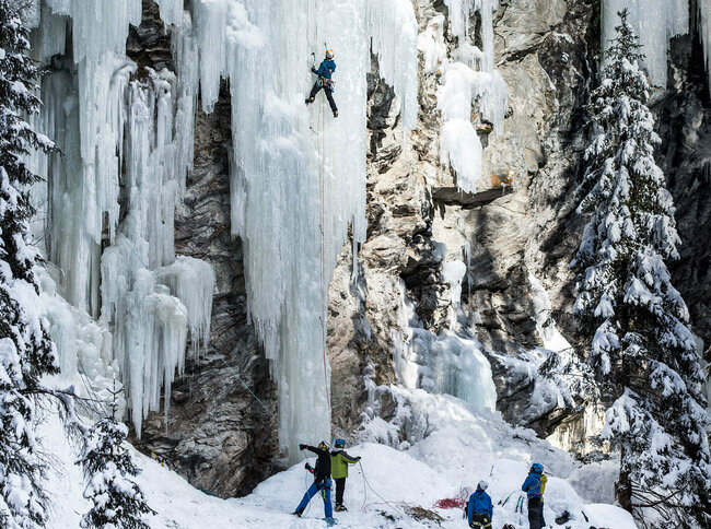 Auf einem gefrorenen Wasserfall klettern mehrere Menschen hoch