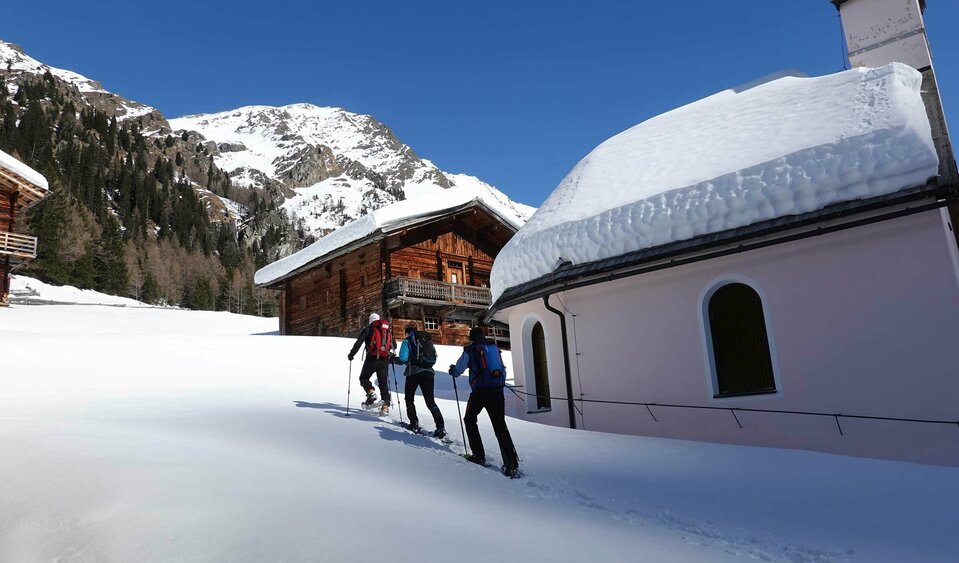 Eine Gruppe beim Schneeschuhwandern, vorbei an einer Kirche im Villgratental