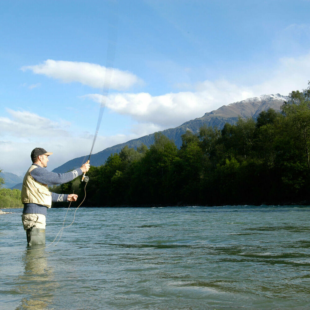 Ein Mann steht in einem Fluss und wirft seine Angel aus zum Fliegen fischen.