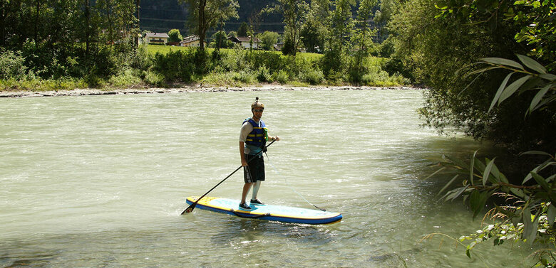 Eine Person mit Schwimmweste und Helm steht auf einem Stand Up Paddle Board auf der Isel.
