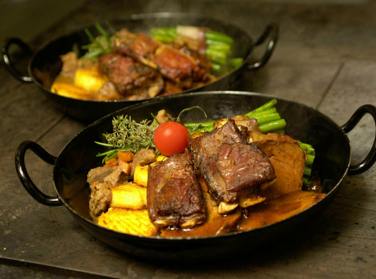 Osttiroler Berglamm mit Speckbohnen und Polenta in einem Eisenpfännchen.