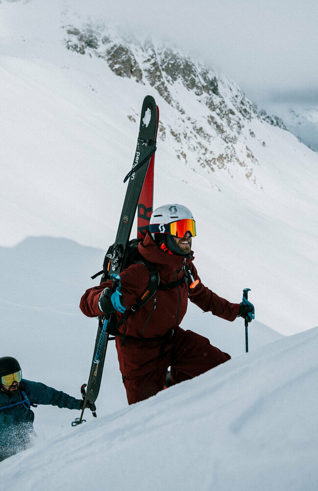 Zwei Skitourengeher befinden sich in einem Steilhang auf ihrer Skitour im Defereggental. Sie tragen ihre Tourenski am Rücken und blicken ihrem Ziel motiviert entgegen.
