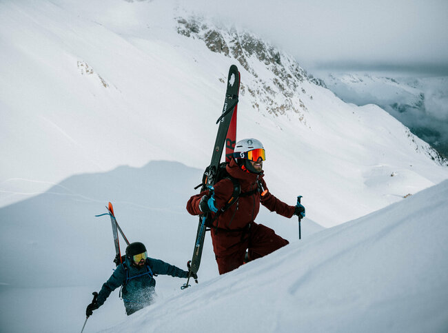 Zwei Skitourengeher befinden sich in einem Steilhang auf ihrer Skitour im Defereggental. Sie tragen ihre Tourenski am Rücken und blicken ihrem Ziel motiviert entgegen.