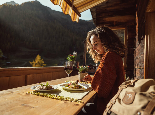Eine Frau genießt eine Portion Schlipfkrapfen auf der Terasse der Unterstaller Alm