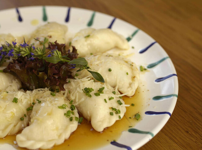 Osttiroler Schlipfkrapfen mit Schnittlauch und geschmolzener Butter auf einem weiß-blauen Teller, mit etwas Salat verziert.