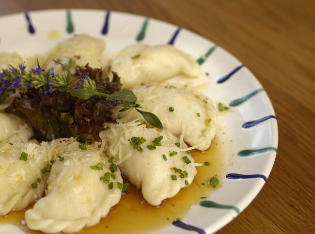 Osttiroler Schlipfkrapfen mit Schnittlauch und geschmolzener Butter auf einem weiß-blauen Teller, mit etwas Salat verziert.
