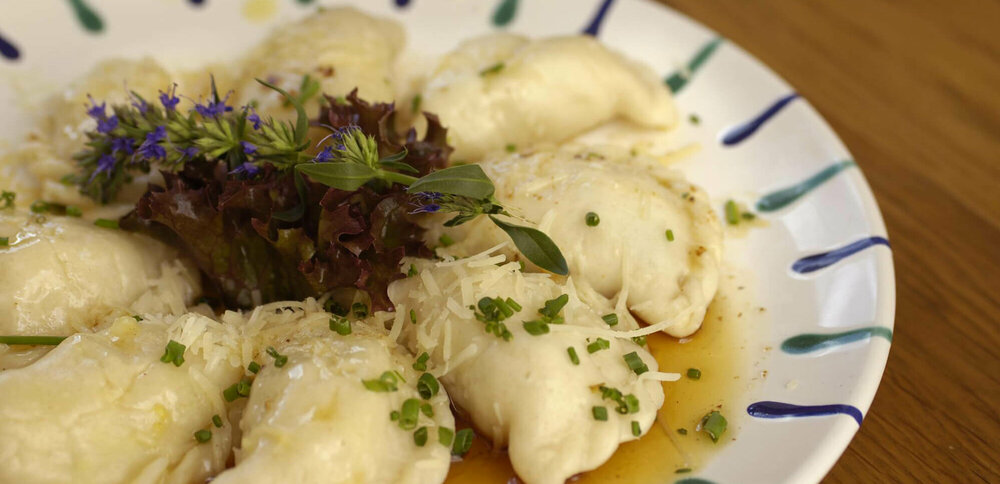 Osttiroler Schlipfkrapfen mit Schnittlauch und geschmolzener Butter auf einem weiß-blauen Teller, mit etwas Salat verziert.