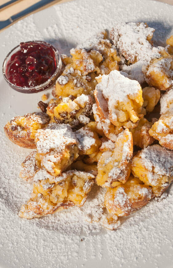 Kaiserschmarren mit Preiselbeeren in einem separaten Schüsselchen auf einem weißen Teller.