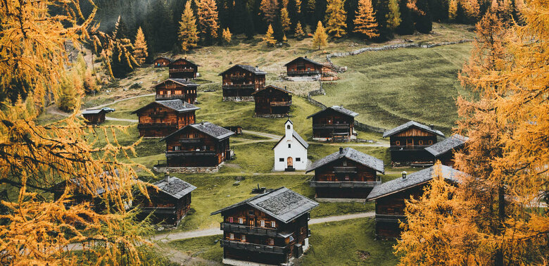 Almhüttendorf "Oberstalleralmen in Innvervillgraten" in herbstlicher Umgebung mit kleiner Kapelle im Zentrum; im Vordergrund goldgelbe Lärchen in Herbstfärbung