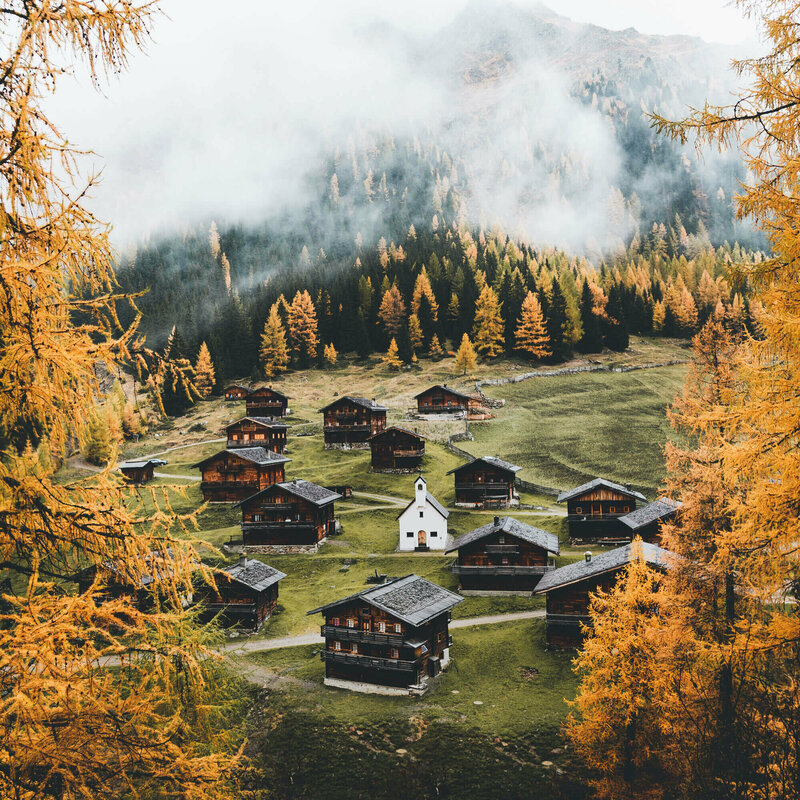 Almhüttendorf "Oberstalleralmen in Innvervillgraten" in herbstlicher Umgebung mit kleiner Kapelle im Zentrum; im Vordergrund goldgelbe Lärchen in Herbstfärbung