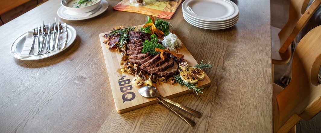 Ein Holzbrett mit einem frisch zubereiteten Hüttengericht steht auf einem Holztisch in der Nilljochhütte. Die Speise ist ansprechend angerichtet