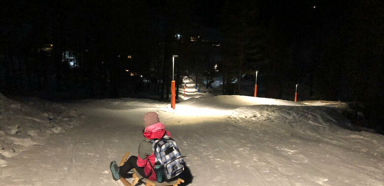 Kind beim Nachtrodeln bei beleuchteter Rodelbahn