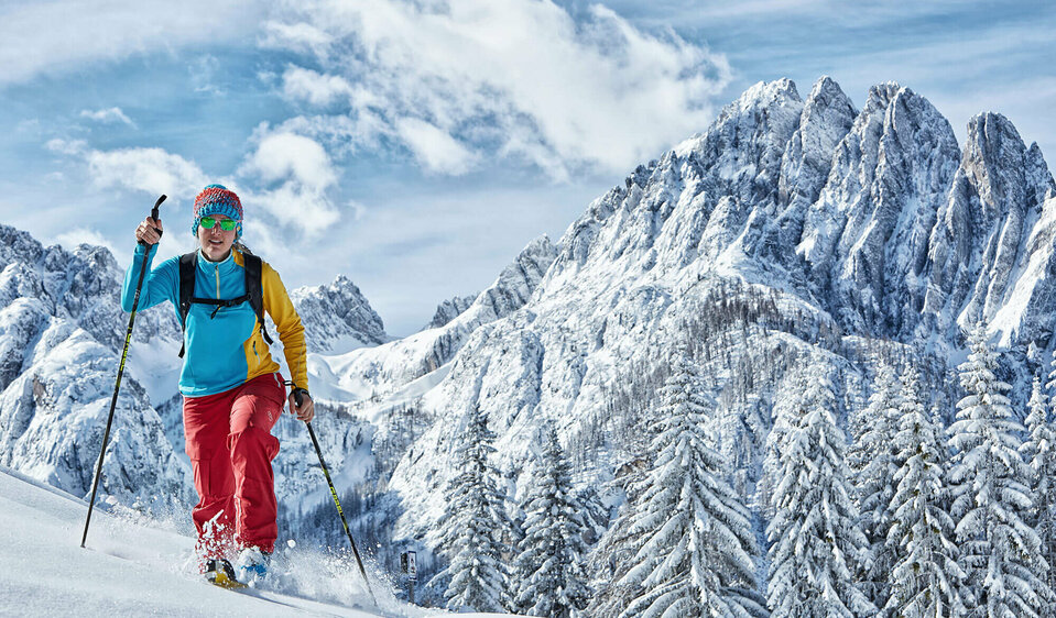 Eine Skitourengeherin mit roter Skihose und blau-gelbem Obertail steigt durch die tief verschneite Landschaft am Auerling in den Lienzer Dolomiten.