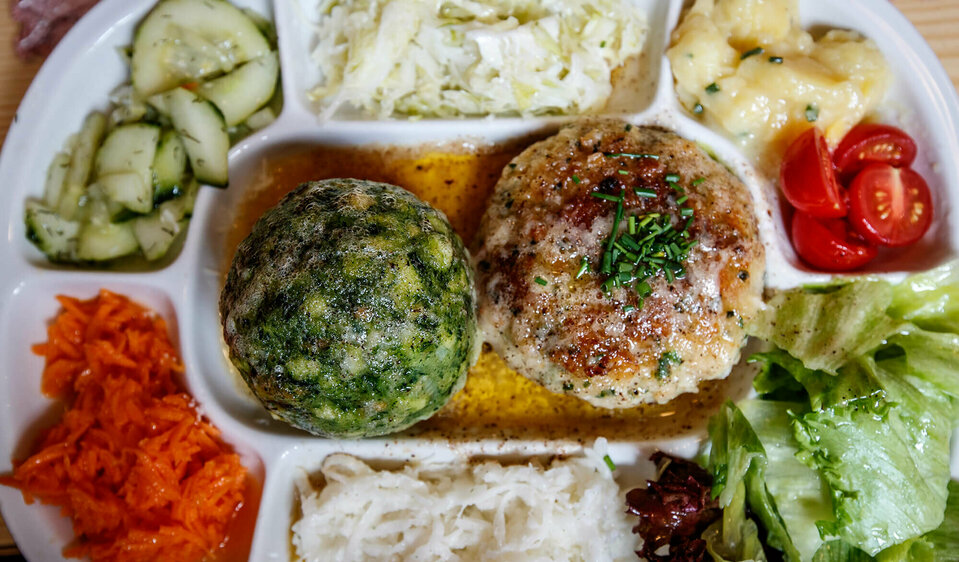 Spinatknödel und Kaspressknödel in brauner Butter. Ringsherum verschiedene bunte Salate auf einem Teller angerichet.
