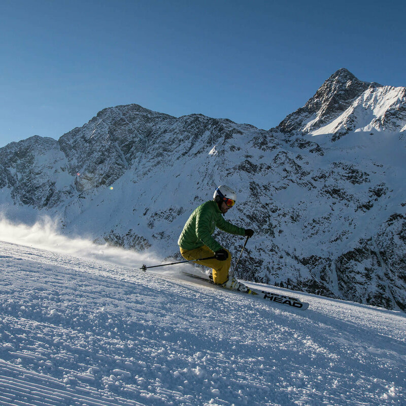 Ein Skifahrer mit grüner Jacke und gelber Hose fährt in sportlichem Fahrstil auf der Abfahrt in Skizentrum St. Jakob im Defereggen.