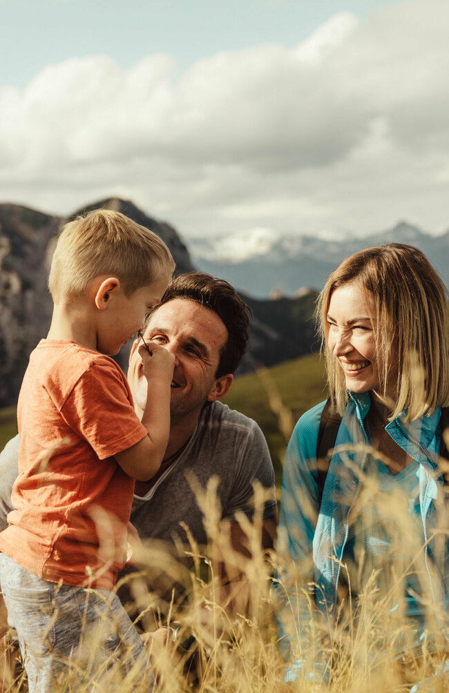 Zu sehen ist ein Elternpaar mit ihrem kleinen Sohn, die im hohen Gras entlang der Kindermeile am Golzentipp den Moment zu dritt genießen.