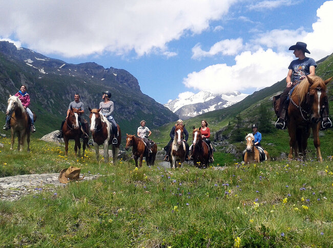 Acht Personen sitzen auf Pferden im Nationalpark Hohe Tauern vor einer Bergkulisse. Im Vordergrund liegt ein Cowboyhut auf dem Boden.