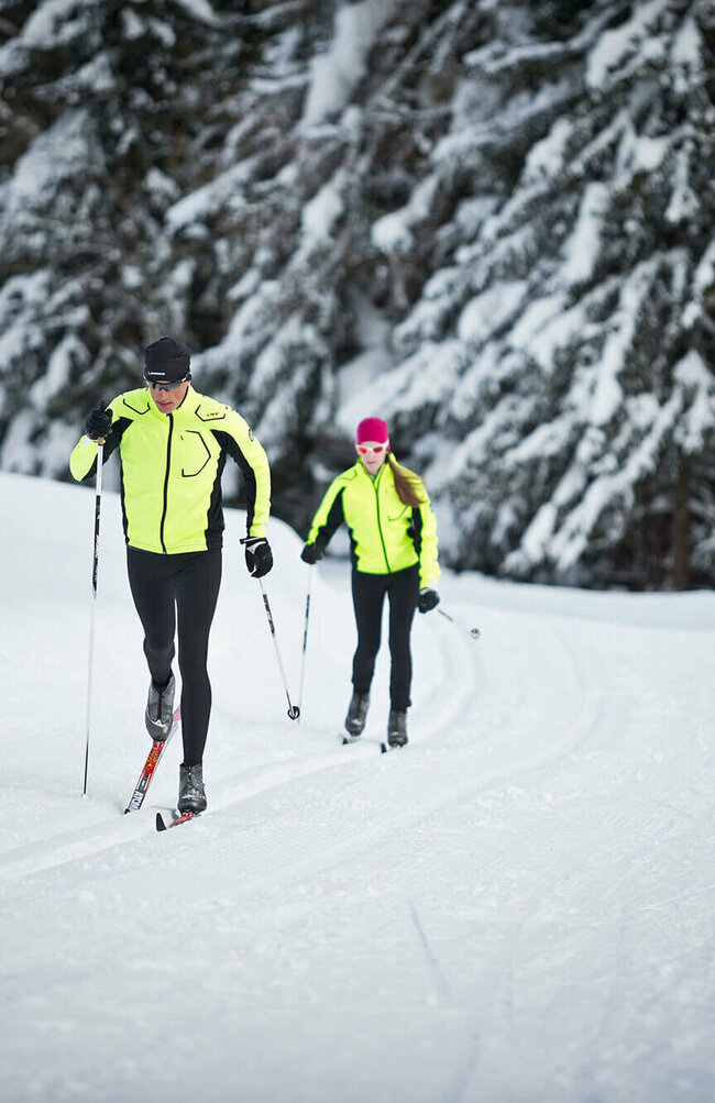 Zwei Langläufer:innen beim Langlaufen auf der Loipe Obertilliach